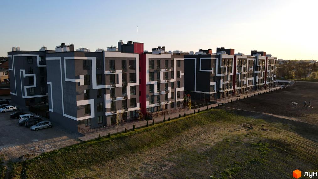 Зовнішній вигляд житлового комплексу Рідний-2 з сірими фасадами та білими декоративними елементами, а також прибудинкова територія з парковкою та зеленими насадженнями.