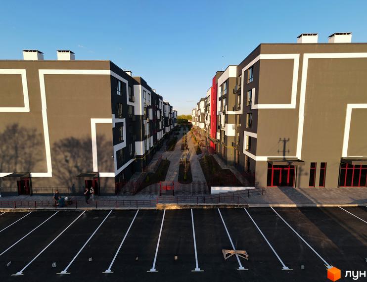 Новобудова ЖК Рідний-2 з сіро-білим фасадом та червоними дверима, що виходить на паркінг з розміткою.