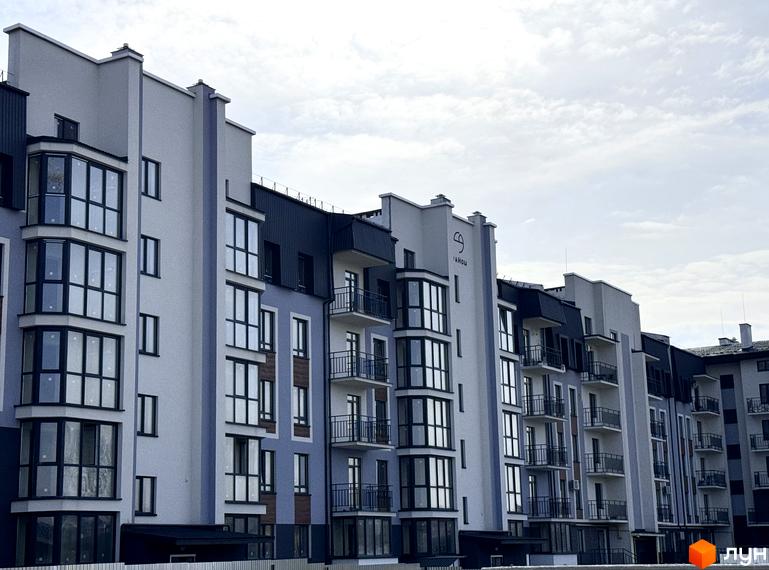 Зовнішній вигляд новобудови ЖК 9 Район з великими вікнами та балконами. Фасад будинку виконаний у світлих тонах з темними елементами.