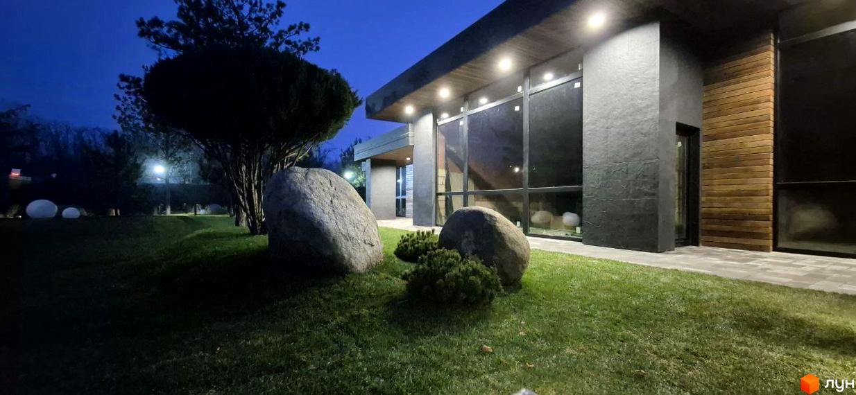 КМ Sobi Life: зовнішній вигляд будівлі з великими вікнами та дерев'яними елементами, прибудинкова територія з газоном та декоративними каменями.