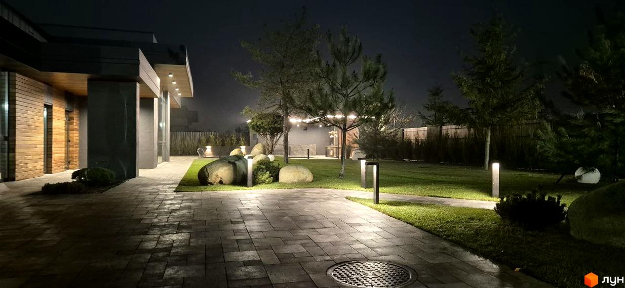 Фасад будинку Котеджного містечка Sobi Life з дерев'яним оздобленням. Прибудинкова територія має бруковані доріжки, газон, дерева та освітлення.