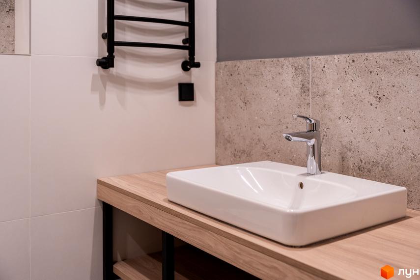 Сучасний дизайн ванної кімнати з білим керамічним умивальником та хромованим змішувачем на дерев'яній стільниці. На стіні розташований чорний полотенцесушитель.