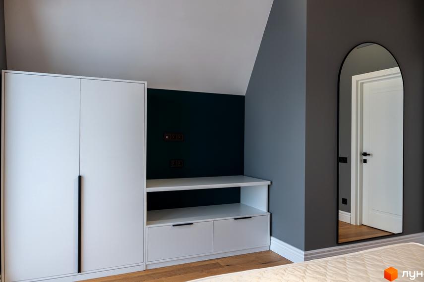 Сучасний інтер'єр спальні з білою шафою та вбудованими меблями. На стіні - дзеркало арочної форми.