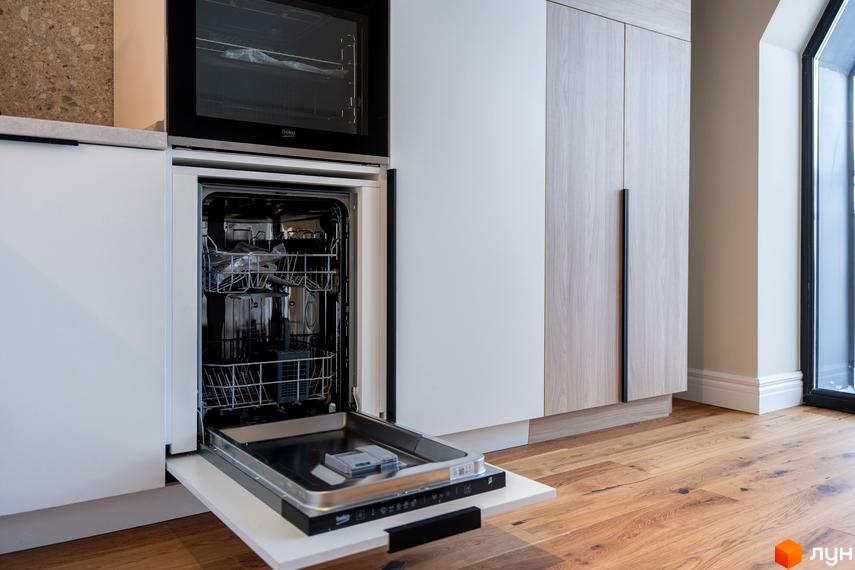 Сучасна кухня з вбудованою технікою: посудомийна машина та духова шафа. Дерев'яні фасади шаф та велике вікно створюють затишну атмосферу.