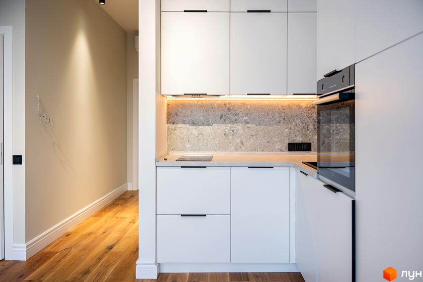 Інтер'єр кухні з білими фасадами, сірим фартухом та дерев'яною підлогою. Сучасний дизайн житлового комплексу AMA FAMILY RESORT.
