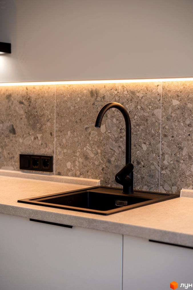 Сучасна кухня з чорною мийкою та змішувачем на тлі сірого керамограніту з підсвічуванням.