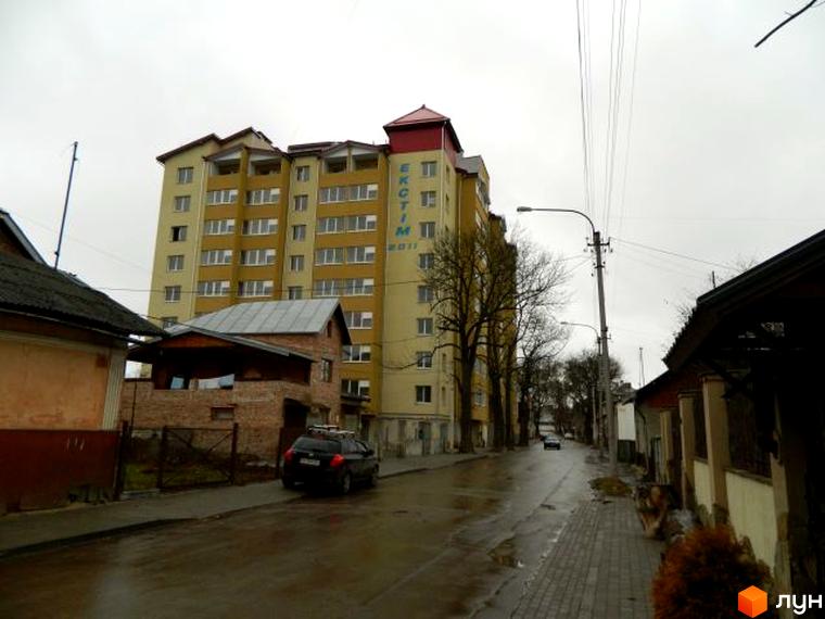 Фото фасаду багатоповерхового будинку по вулиці Ольги Кисілевської, 10. На передньому плані вулиця з припаркованим автомобілем.