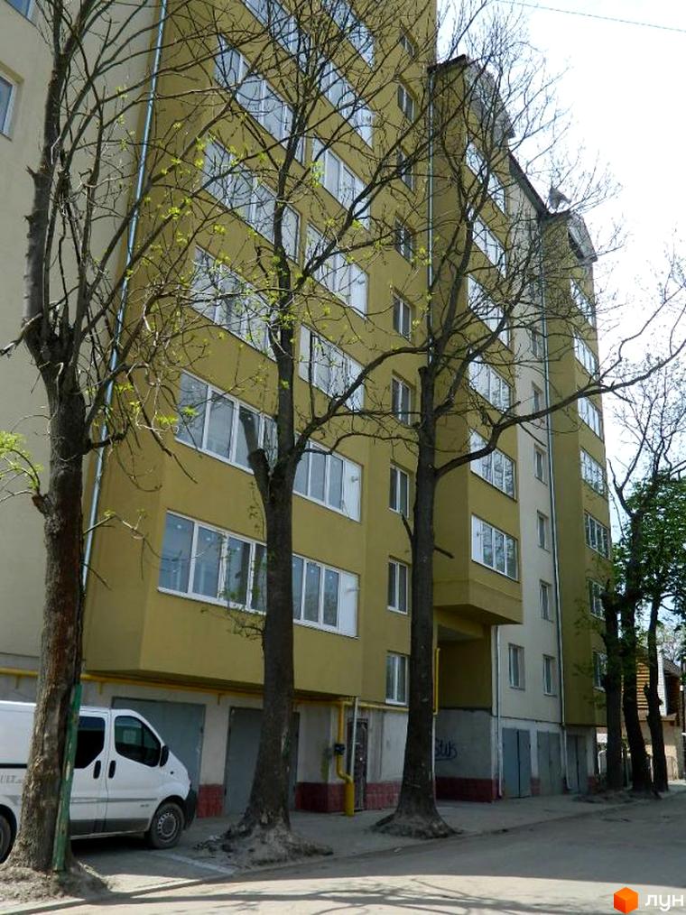 Зовнішній вигляд будинку на вулиці Ольги Кисілевської, 10. Багатоповерхова будівля з великими вікнами та деревами перед нею.