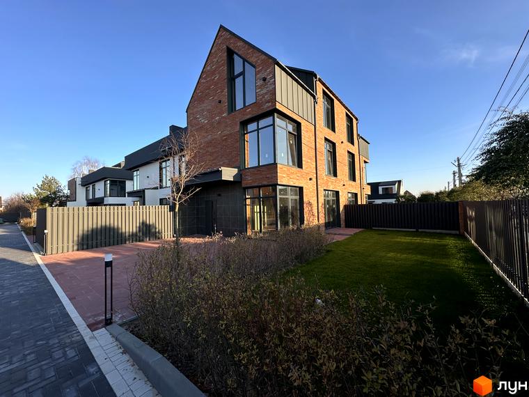 Таунхауси Lagom House з червоної цегли під блакитним небом. Прибудинкова територія з зеленим газоном та доріжками з бруківки.