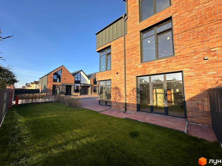Зовнішній вигляд таунхаусів Lagom House з червоної цегли та металевих елементів, зелений газон та доріжка з бруківки.