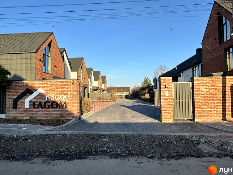 Таунхауси Lagom House з цегляним фасадом та сірим дахом розташовані вздовж вимощеної бруківкою алеї.