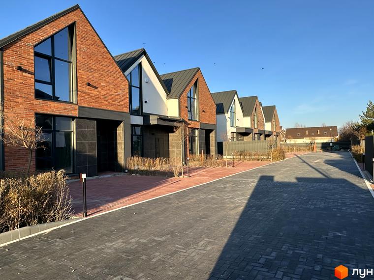 Таунхауси Lagom House з червоної цегли та білою штукатуркою під блакитним небом. Повністю вимощена сірою бруківкою прибудинкова територія та зелені насадження.