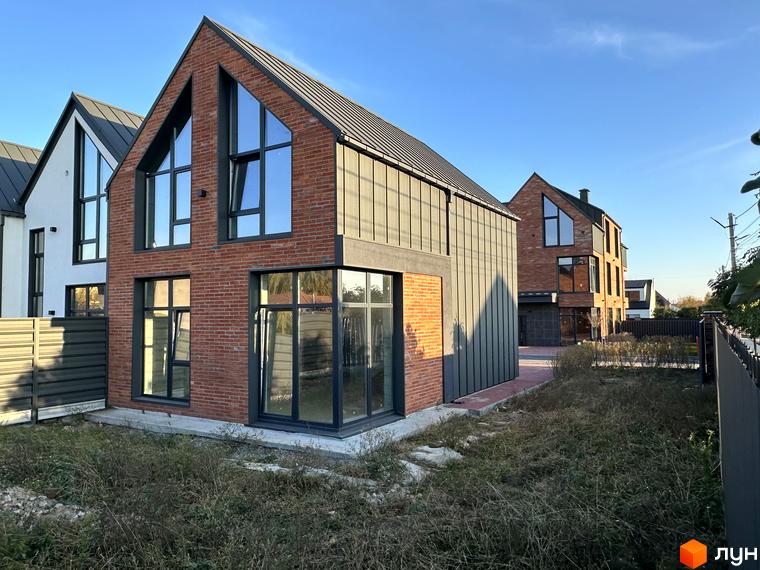 Таунхауси Lagom House з червоної цегли та сірого металу з великими вікнами. Навколо будівель зелень та паркан.