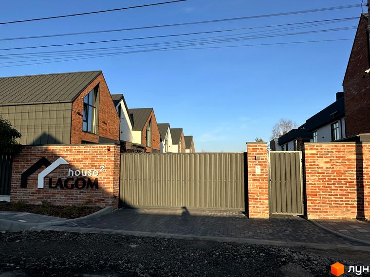 Вхідна група та сучасні таунхауси Lagom House з цегляним фасадом та темним дахом. Огороджена територія з бруківкою.