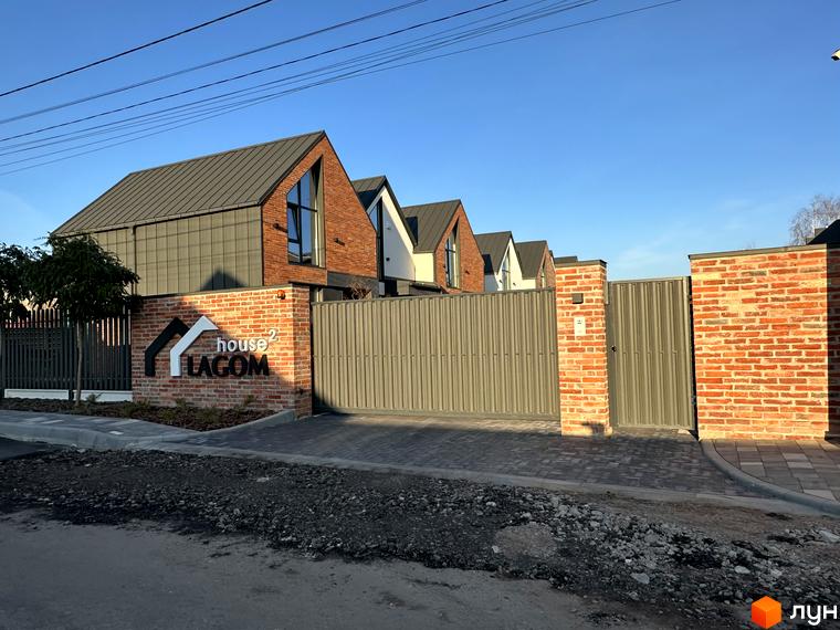 Таунхауси Lagom House з цегляним фасадом та сірим дахом. Прибудинкова територія з бруківкою та огорожею.