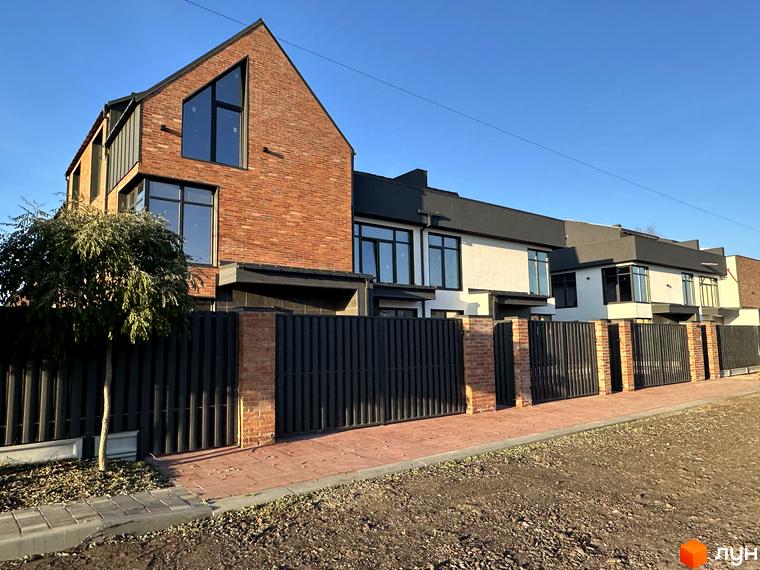 Таунхауси Lagom House з цегляним фасадом та великими вікнами, огороджені парканом з цегляними колонами та металевими секціями.