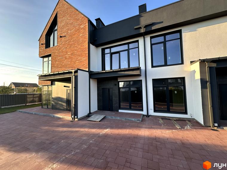 Таунхауси Lagom House з цегляним фасадом та білими стінами, з великими чорними вікнами, на тлі блакитного неба. Перед будинком викладена червона бруківка.