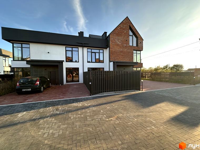 Зовнішній вигляд таунхаусів Lagom House з цегляним фасадом та білими стінами, прибудинкова територія з бруківкою та парканом.