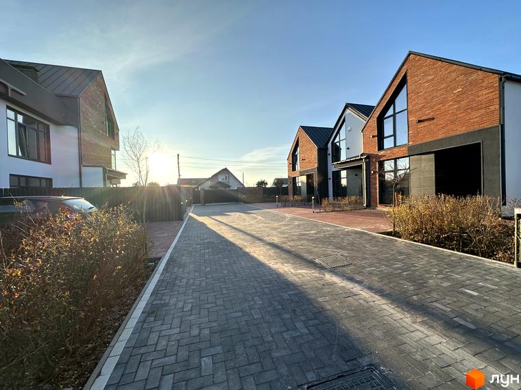 Таунхауси Lagom House з цегляним фасадом та великими вікнами, розташовані на вимощеній сірою плиткою території з кущами.