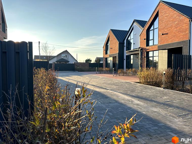 Таунхауси Lagom House з червоної цегли з великими вікнами на тлі блакитного неба. Перед будинками вимощена сіра плитка та зелені кущі.