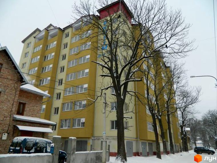 Зображення фасаду будинку по вулиці Ольги Кисілевської, 10. Багатоповерхова будівля з великою кількістю вікон та деревами навколо.