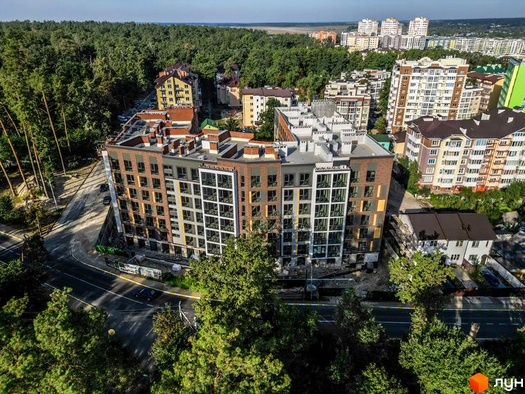 Житловий комплекс GL Club: багатоповерховий будинок з вигнутим фасадом, оздоблений цеглою та панелями. Розташований біля лісу та дороги.
