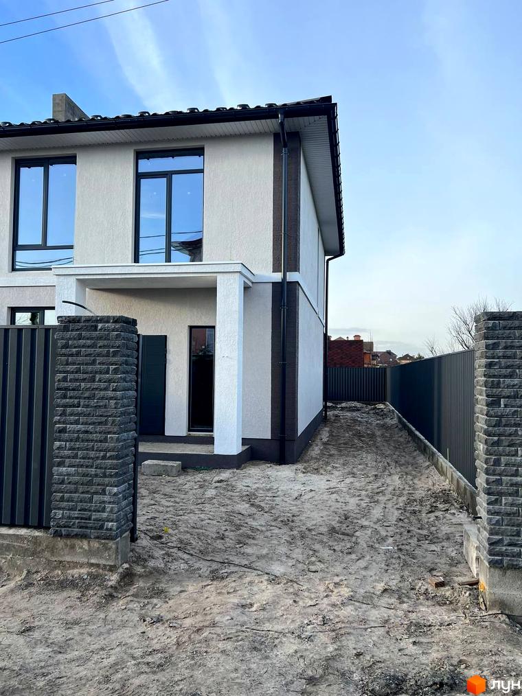 Зовнішній вигляд дуплексу Four story з цегляними колонами та огорожею. Прибудинкова територія з піщаною дорогою та парканом.