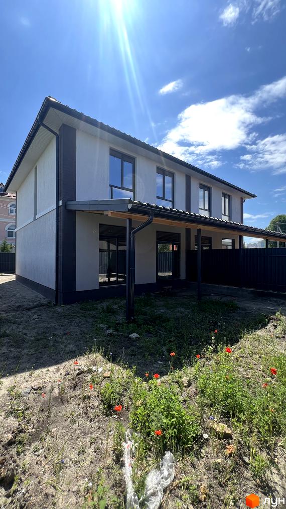 Двоповерховий дуплекс з сірим фасадом та великими вікнами під блакитним небом. Навколо будинку зелена ділянка з червоними квітами.