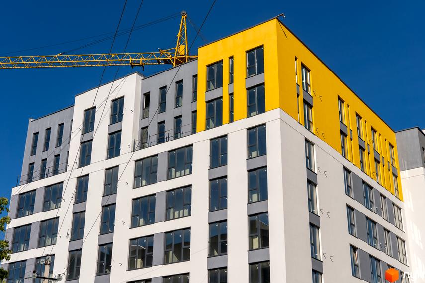 Новобудова ЖК Весняний з яскравою жовтою секцією та великою кількістю вікон під блакитним небом. Будівельний кран на фоні.