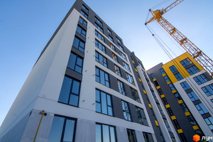 Зовнішній вигляд новобудови ЖК Весняний з панорамними вікнами та яскравими жовтими акцентами. Будівельний проєкт знаходиться під наглядом крана.