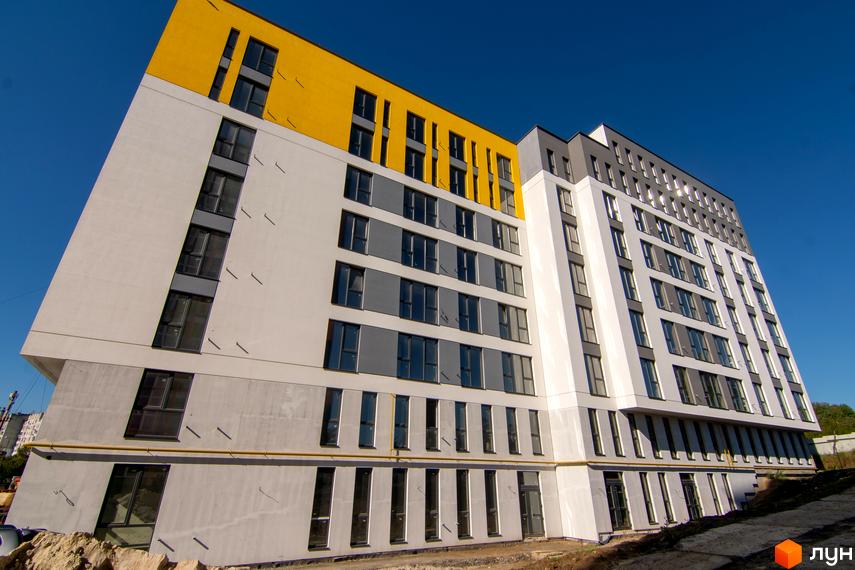 Житловий комплекс Весняний - фасади будівлі з білими, сірими та жовтими елементами, великою кількістю вікон. Будівельний проєкт розташований на фоні блакитного неба.