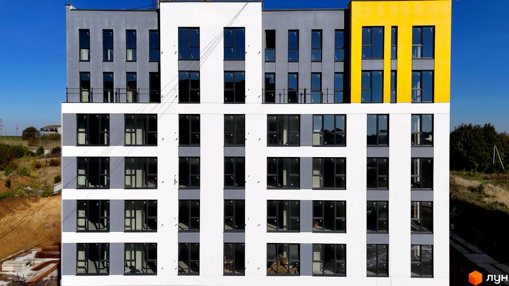 Фасад житлового комплексу Весняний з великою кількістю вікон та балконів, поруч територія будівництва.