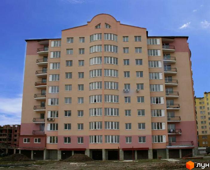 Зображення фасаду багатоповерхового будинку на вул. Хіміків, 25. Житловий комплекс з балконами та великими вікнами на фоні блакитного неба.