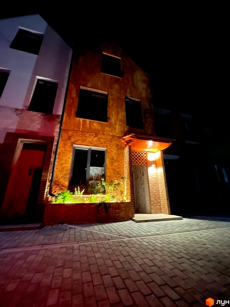 Котеджне містечко KADENYUK homes вночі. Зовнішній вигляд будинку з цегляною кладкою та підсвічуванням. Прибудинкова територія з бруківкою.
