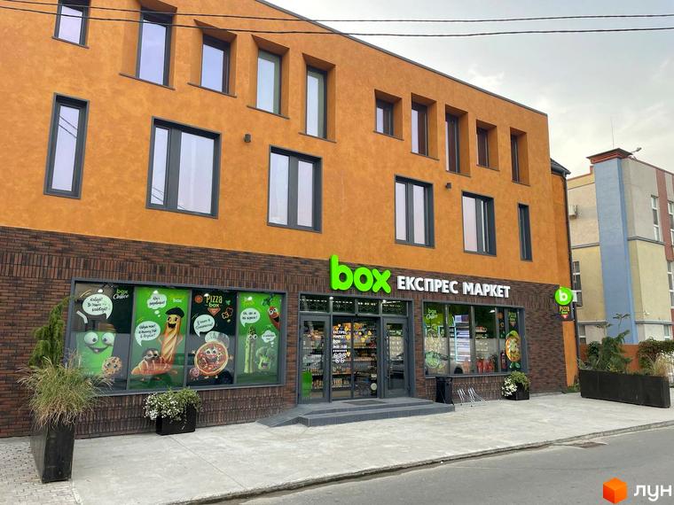 Зовнішній вигляд фасаду будинку з оранжевою штукатуркою та цегляною основою, вікнами різних розмірів та вивіскою 