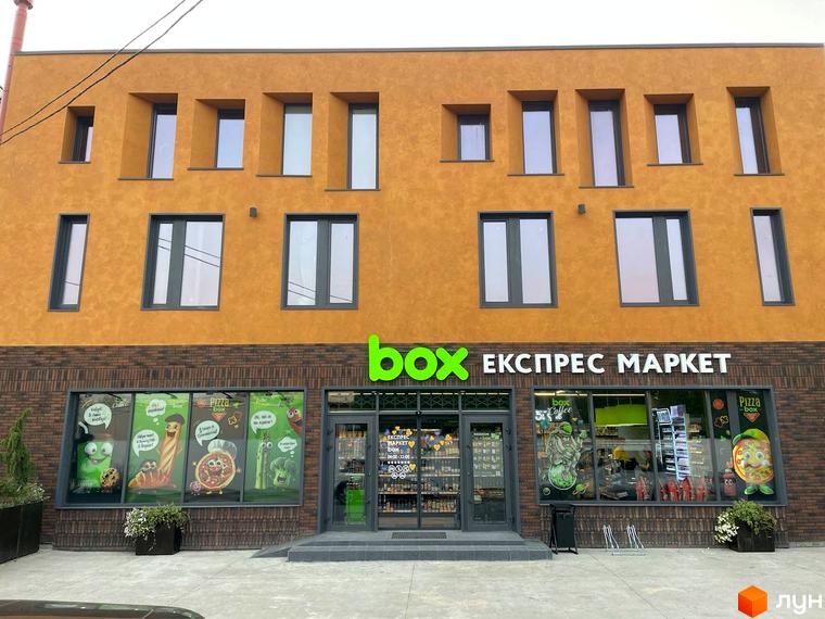 Будинок житлового комплексу КМ КАDЕНЮК homes з фасадом жовтого кольору та цегляною обробкою цоколя. Перед фасадом розташована прибудинкова територія з зеленими насадженнями.