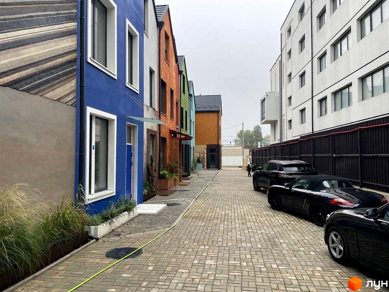 Котеджне містечко KADENIUK homes з яскравими фасадами будинків та вимощеною бруківкою прибудинковою територією з припаркованими автомобілями.