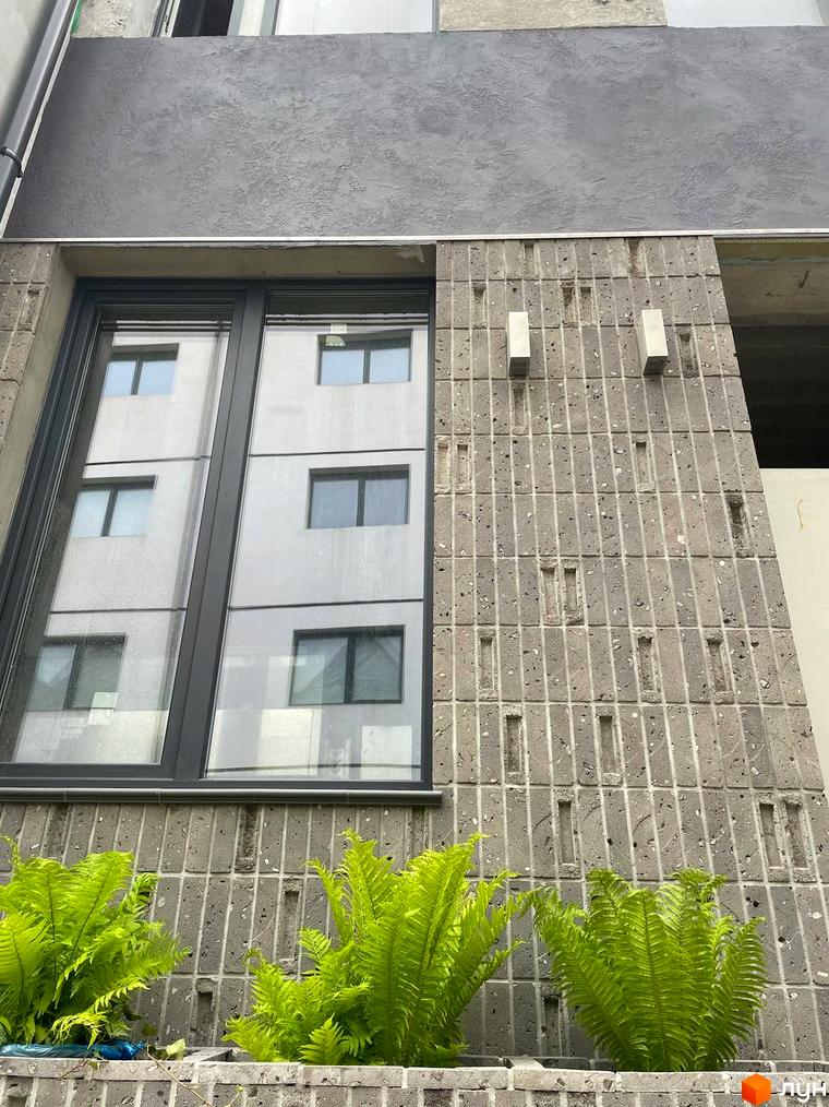 Фасад житлового комплексу КМ KADENIUK homes з вікнами та текстурною плиткою, зелені рослини біля будинку.