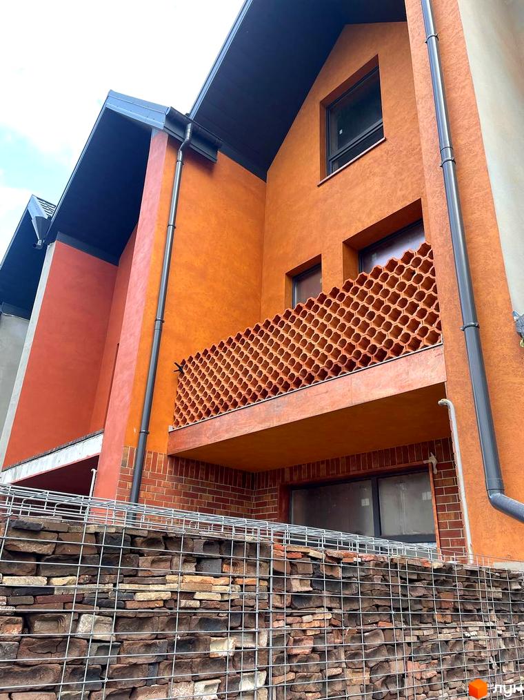 Зовнішній вигляд будинку КМ КАDЕНЮК homes з оранжевим фасадом, балконом з декоративною решіткою та кам'яним парканом.