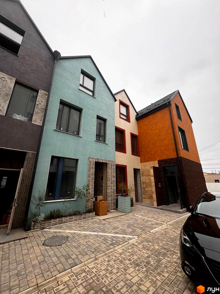 Фасад будинку КМ KADENYUK homes з різнокольоровими стінами та бруківкою на прибудинковій території. Сучасна архітектура новобудови.