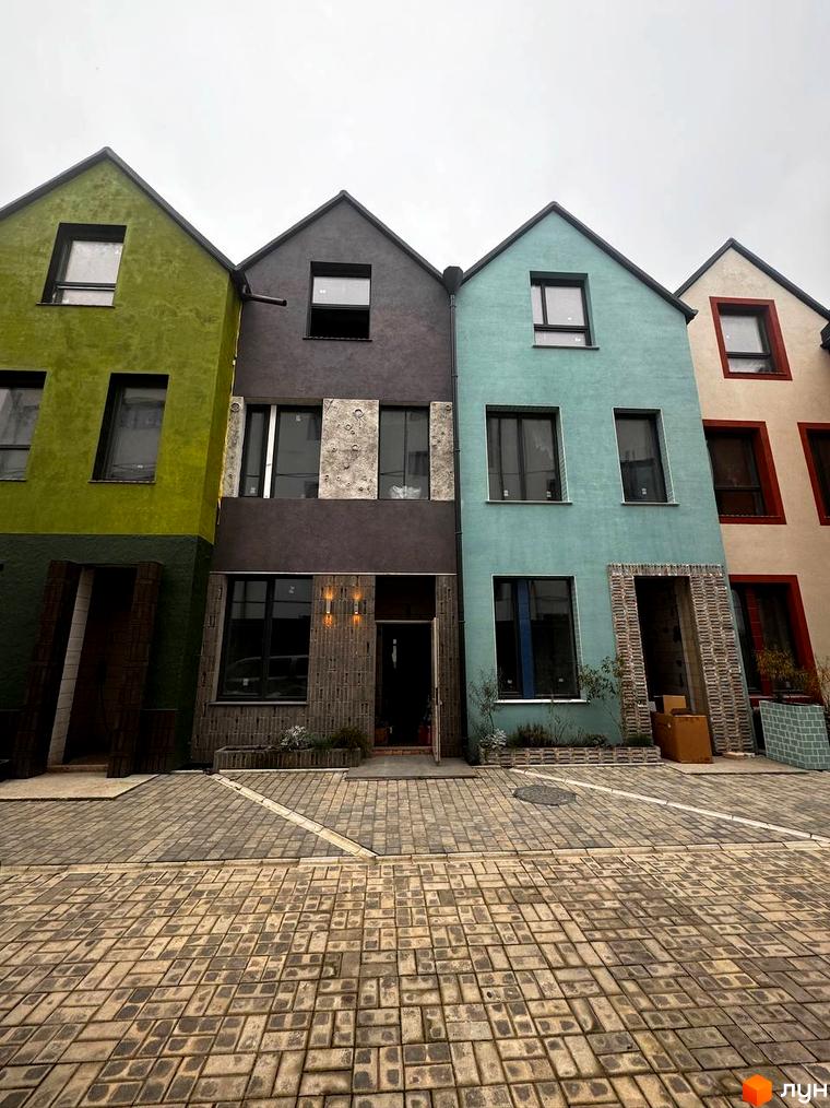 Котеджне містечко KADENYUK homes: фасади будинків у зеленій, сірій та бірюзовій кольорах з великими вікнами, вимощена бруківкою прибудинкова територія.