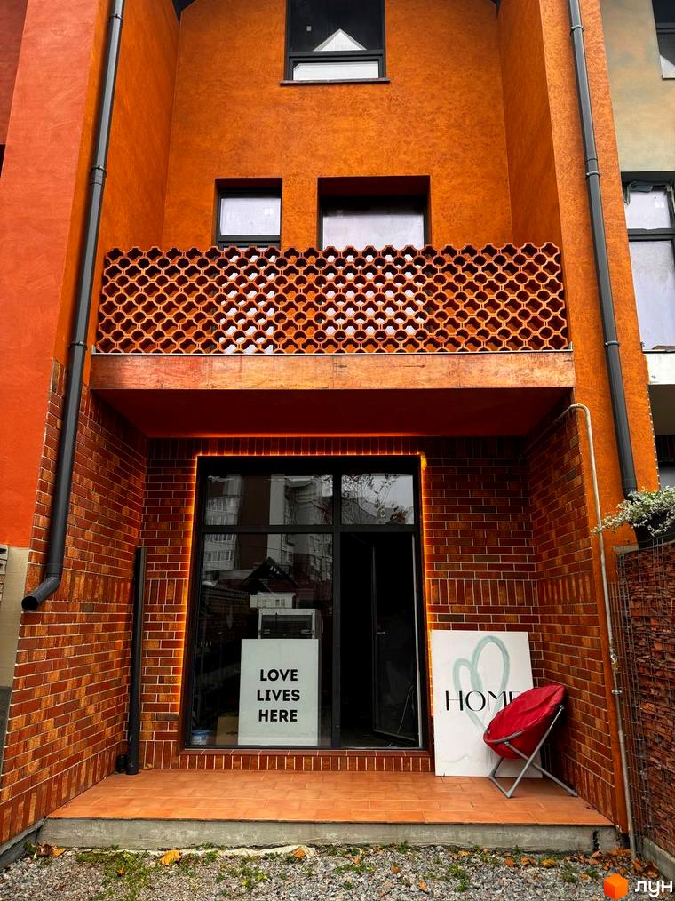 Фасад будинку житлового комплексу КМ КАDЕНЮК homes з цегляною кладкою та вікнами. Поруч розташована червона крісло та вивіска HOME.