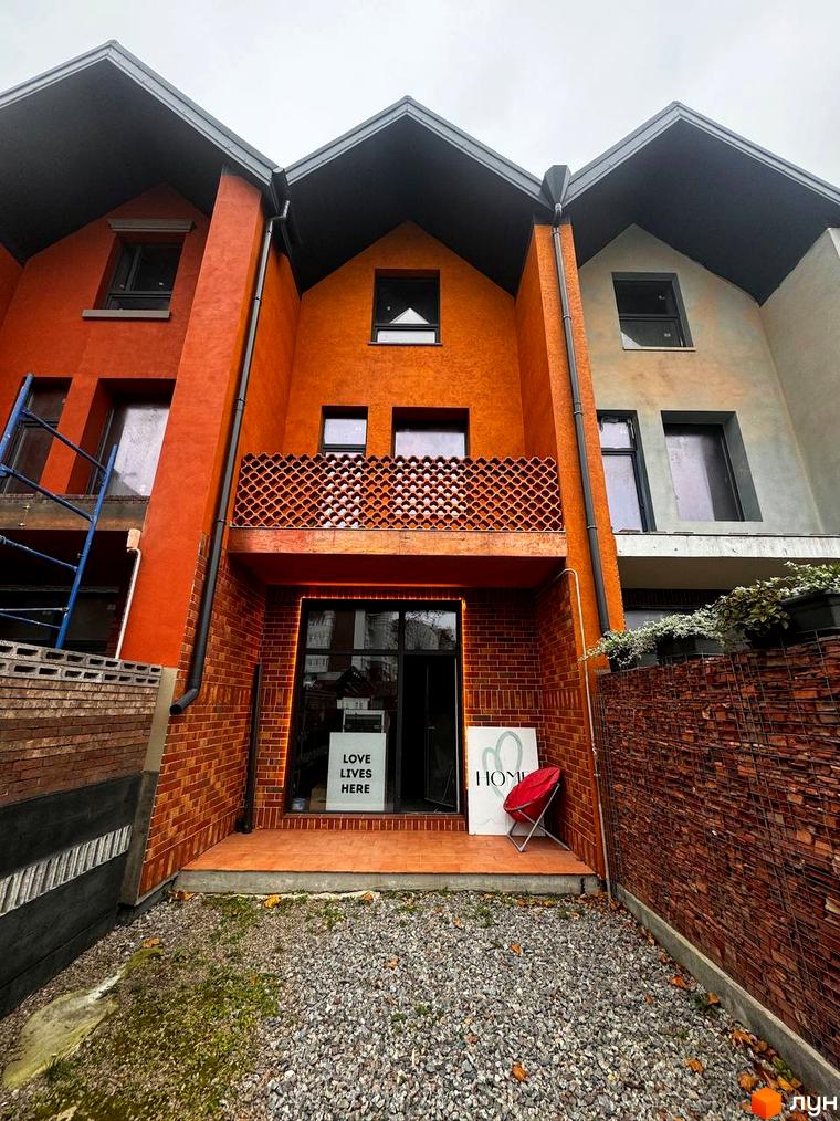 Котеджне містечко KADENYUK homes: фасади будинків з цегли та штукатурки, вікна, балкон з візерунком, вхідна група, червоне крісло, зелень, гравій.