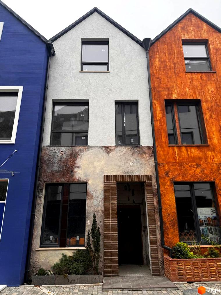 Фасад житлового комплексу КМ КАDЕНЮК homes з різнокольоровими стінами та вікнами. Навколо будинку облаштована прибудинкова територія з рослинністю.