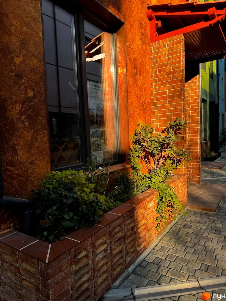 Котеджне містечко KМ KADENIUK homes з фасадом з червоної цегли та декоративною штукатуркою, прибудинкова територія з бруківкою та зеленими насадженнями.