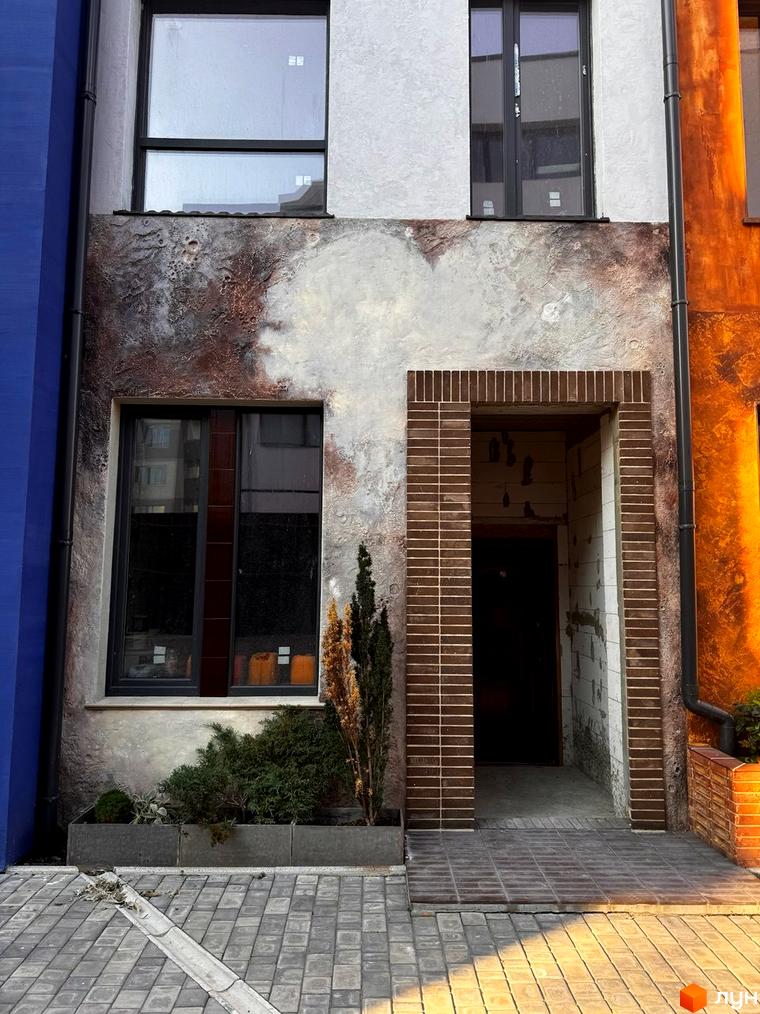 Котеджний комплекс КАDЕНЮК homes з унікальним фасадом та вхідною групою. Прибудинкова територія з доглянутими рослинами та бруківкою.