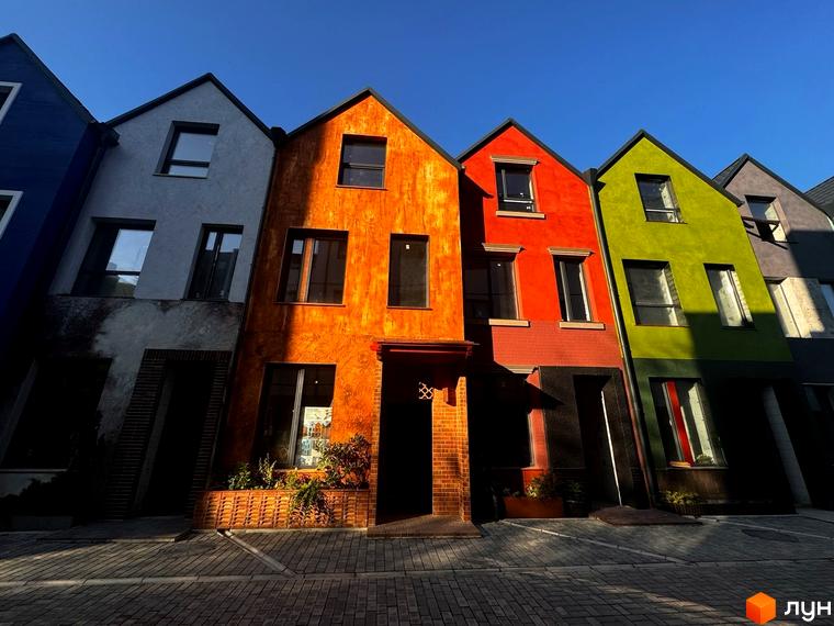 Котеджне містечко KADENYUK homes з яскравими фасадами будинків та брукованою прибудинковою територією. Зовнішній вигляд будинків у різноманітних кольорах підкреслює їхню індивідуальність.