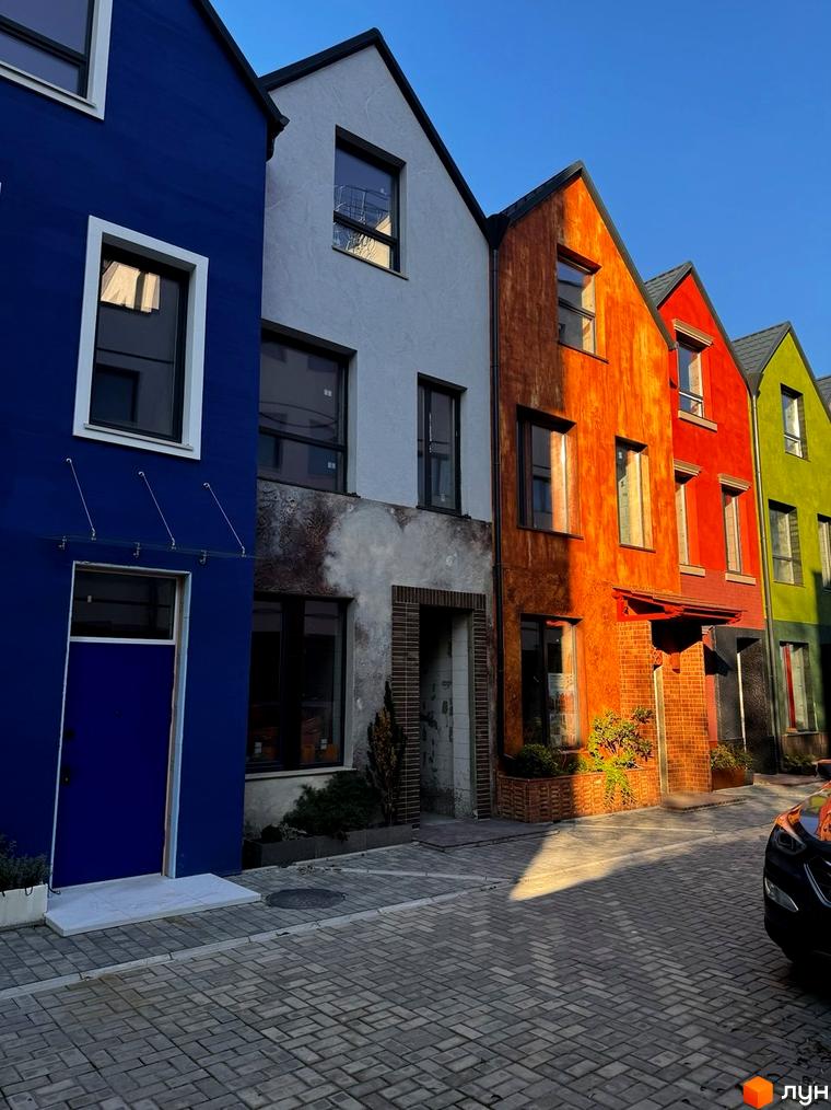 Котеджне містечко КАDЕНЮК homes: яскраві фасади будинків синього, сірого, помаранчевого, червоного та зеленого кольорів, вимощені бруківкою вулиці та прибудинкова територія.