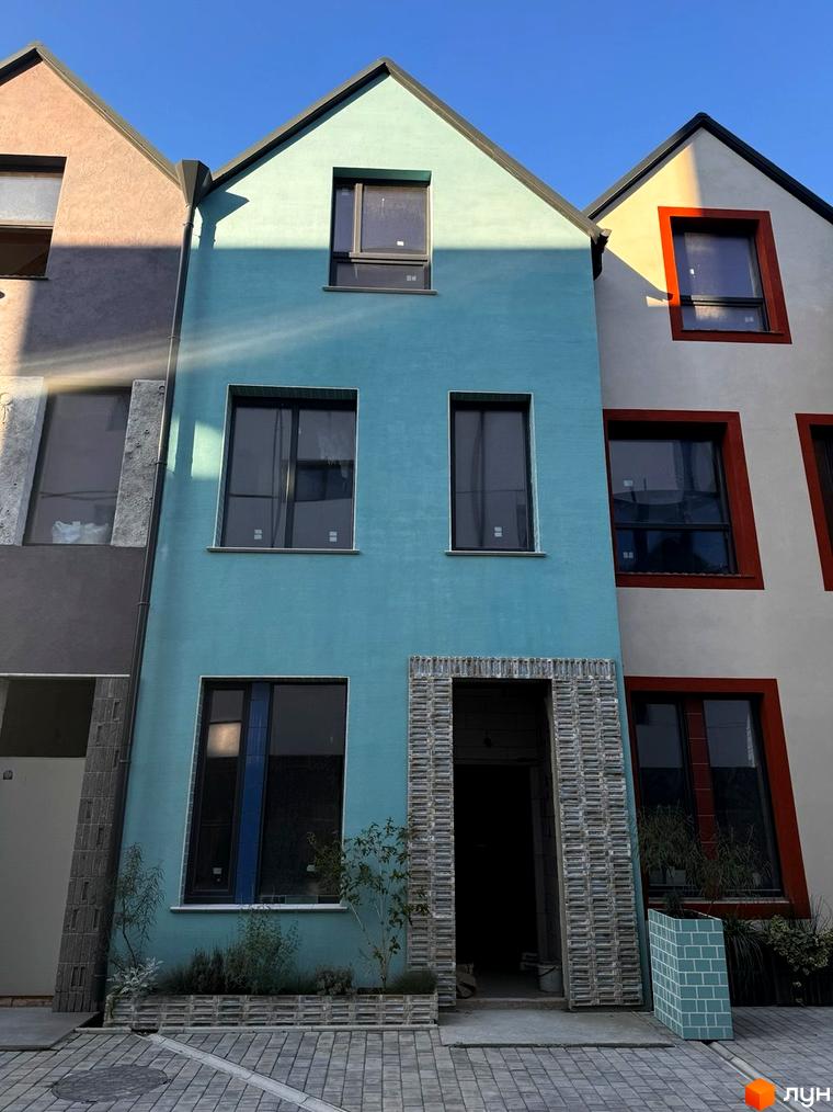 Котеджне містечко KADENIUK homes: фасади будинків у блакитному та білому кольорах з червоними акцентами, вхідна група оздоблена плиткою, перед будинками облаштована прибудинкова територія.