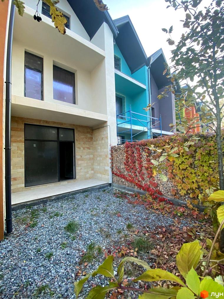 Зовнішній вигляд будинку КМ KADENYUK homes з цегляним фасадом та великим вікном. Прибудинкова територія з гравієм та зеленню.